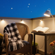 Cozy balcony with warm autumn outdoor lighting ideas, featuring a chair, blanket, flowers, and a table with a book.